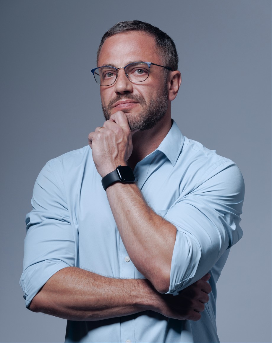 Fabio Fares de camisa social clara, braços cruzados e a mão no queixo